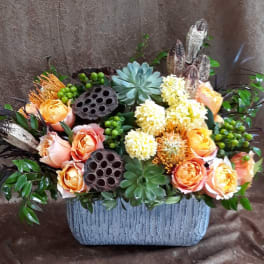 Arrangement of peach roses and pale yellow blooms in a textured gray container