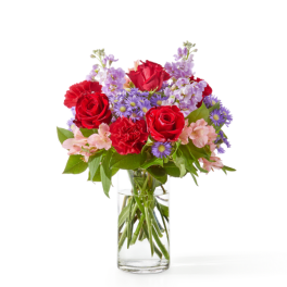 Mixed bouquet of red roses and carnations with purple and pink blooms in a clear glass vase