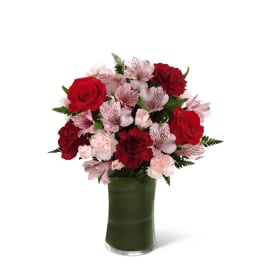Red roses and pink flowers arranged in a green glass vase