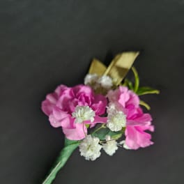 Pink carnation and white filler flower boutonniere with gold ribbon and pearl pin on a dark background