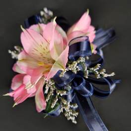 Pink alstroemeria corsage with navy ribbon on a dark background