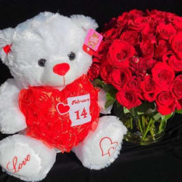White teddy bear beside a bouquet of red roses