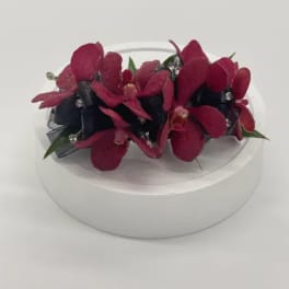 Red orchid wrist corsage with black ribbon and rhinestone accents on a white stand