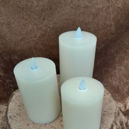 Three white pillar candles with faux flames on a textured brown surface