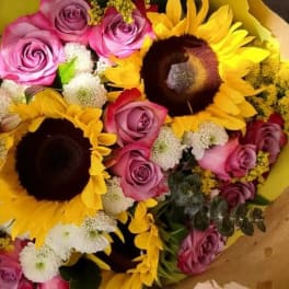 Bouquet of pink roses, sunflowers, and white pom flowers wrapped in yellow paper