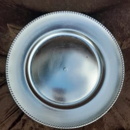 Round silver charger plate with beaded rim on a dark fabric background