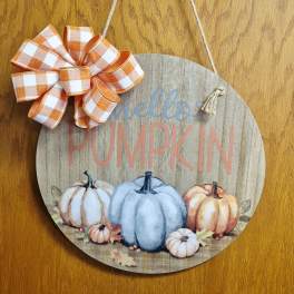 Round wooden pumpkin sign with orange plaid bow hanging by twine