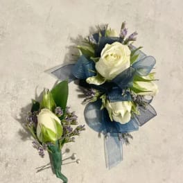 White rose corsage and matching boutonniere with blue ribbon and small purple flowers.