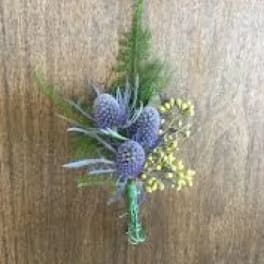 Small boutonniere of purple thistle-like blooms with yellow accents and greenery tied with green tape