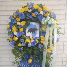 Standing floral wreath with blue and yellow flowers and a bear tribute card