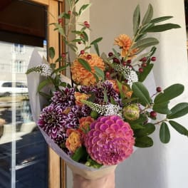 Handheld bouquet of pink, orange, and purple flowers with greenery