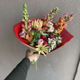 Handheld bouquet with mixed pink, red, and yellow flowers wrapped in red paper