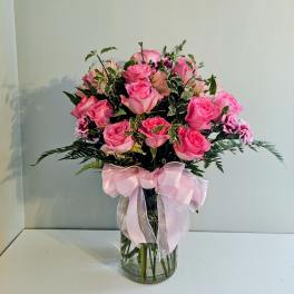 Pink roses arranged in a clear glass vase with a pink ribbon
