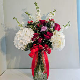 Red roses and white hydrangeas in a clear glass vase with a red ribbon