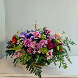 Mixed bouquet of pink and purple flowers in a basket with a purple ribbon
