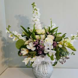 White floral arrangement in a speckled vase with a white ribbon