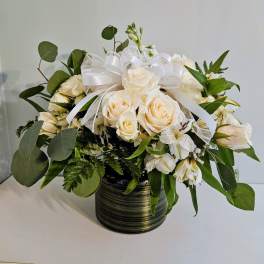 Cream roses and white flowers in a dark striped vase with a white ribbon