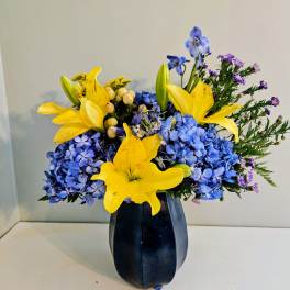 Blue hydrangeas and yellow lilies arranged in a dark vase