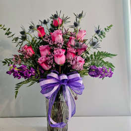 Pink and purple rose bouquet in a clear glass vase with a purple ribbon