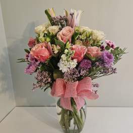 Mixed bouquet of pink and white flowers in a glass vase with a pink ribbon