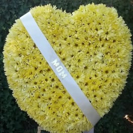 Heart-shaped yellow chrysanthemum wreath with a white ribbon reading MOM