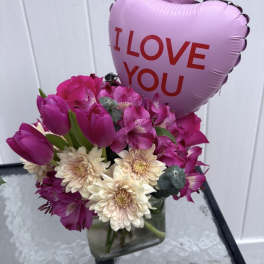 Pink bouquet with tulips and daisies in a glass vase, topped with a heart balloon
