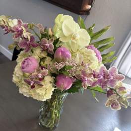 Bouquet of pink peonies, white hydrangeas, and spotted orchids in a glass vase