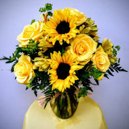 Yellow roses and sunflowers arranged in a glass vase