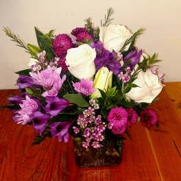 Bouquet of white roses, purple flowers, and pink blooms in a glass vase