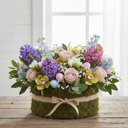 Pastel flower arrangement in a moss-covered round box with decorative eggs