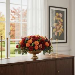 Low floral centerpiece in a gold pedestal bowl with red and orange blooms