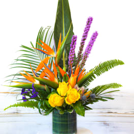 Tropical arrangement with yellow roses and orange bird-of-paradise in a glass vase