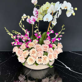 Arrangement of pale roses and orchids in a low round container