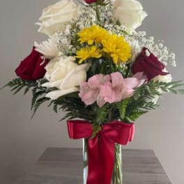 Mixed bouquet of roses, daisies, and pink flowers in a glass vase with a red bow
