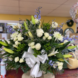 White and blue floral arrangement in a white vase with a silver bow
