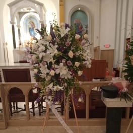 Large standing floral spray with white lilies and purple flowers on an easel