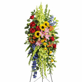 Tall standing floral spray with red roses, sunflowers, lilies, and blue flowers