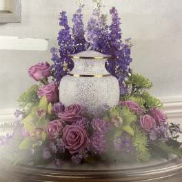 Purple roses and flowers arranged around a white urn on a table