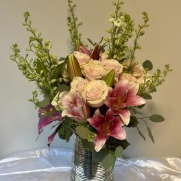 Pink lilies and pale roses arranged in a striped metal vase