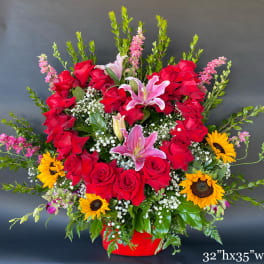 Large red rose and pink lily arrangement with sunflowers in a red container
