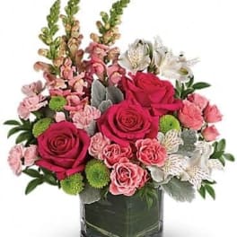 Pink roses and mixed blooms arranged in a square glass vase