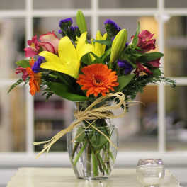 Bouquet of yellow lilies, orange gerbera daisies, and pink alstroemeria in a glass vase