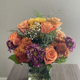 Orange and purple mixed flowers arranged in a square glass vase