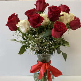 Arrangement of red and white roses with baby's breath in a clear glass vase tied with a red ribbon.