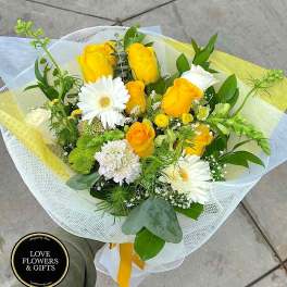 Hand-tied bouquet of yellow roses and white gerbera daisies wrapped in white and yellow mesh.