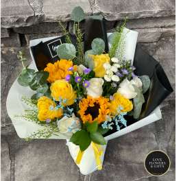 Hand-tied bouquet with sunflowers, yellow and white roses, and purple asters in paper wrap