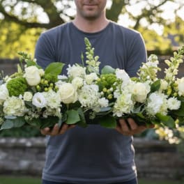 Man holding a long white floral arrangement with roses and snapdragons