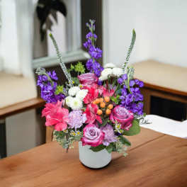 Mixed pink, purple, and white flowers arranged in a white vase
