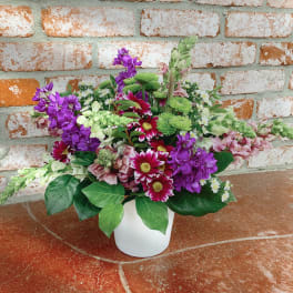 Mixed bouquet of purple, pink, white, and green flowers in a white vase