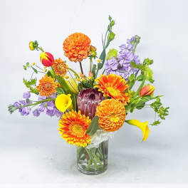 Colorful mixed bouquet in a clear glass vase with orange, purple, yellow, and white blooms